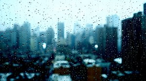 Rain drops pouring down on window glass with urban city skyline view on a rainy weather day