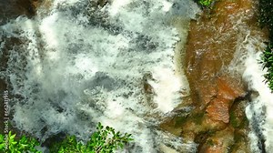 A secluded waterfall in a pristine rainforest, its layers of water gracefully tumble down moss-covered rocks. Witness the serene beauty, thanks to a drone's aerial perspective. Thailand.