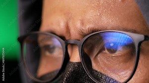 macro view of computer hacker's eye with glasses looks at monitors while doing cyber crimes
