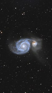 M51 – INTERACTING GALACTIC STRUCTURE M51, the Whirlpool Galaxy, is a grand-design spiral undergoing a close gravitational encounter with its companion NGC 5195. This interaction pulls out long tidal streams, compresses gas in the spiral arms, and ignites bursts of star formation that trace the galaxy’s sweeping blue structure. The distorted dust lanes and extended tidal debris record multiple past passages of the companion, each reshaping M51’s disk and amplifying its spiral density waves. The s