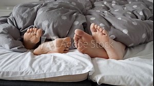 Closeup of couple's feet lying on bed and gently touching each other. Concept of love, relations and having good time together