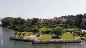 Establishing view of lakeside resort Il sole di Ranco restaurant from Lake Maggiore with picturesque manicured green landscape, park and waterfront property, Italy, overhead aerial circle approach