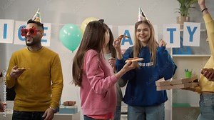 Modern office workers dancing eat pizza. A group of young people in party hats and accessories in the office at a party. Close up. Party, birthday, office party.
