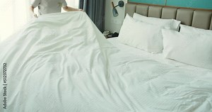 Youngs hard-working females housekeeper in uniform getting luxury hotel room ready by changing white linens while making bed