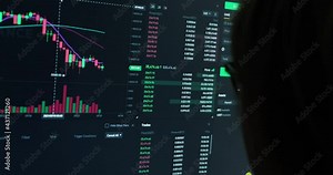 Monitor with live updating crypto prices with green and red indicators, financial charts of bitcoin, online investing platform, person with eyeglasses silhouette in front.