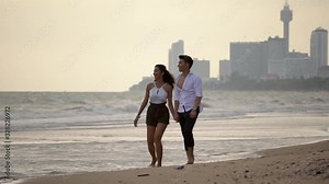young happy people spending their time by ocean, guy in white shirt holding his girlfriend's hand, pointing to horizon romantic eveing on the beach