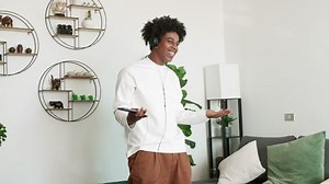 Happy funny generation z hipster African American guy wearing headphones dancing at home, listening music on mobile phone, having fun feeling funky moving in slow motion in living room.