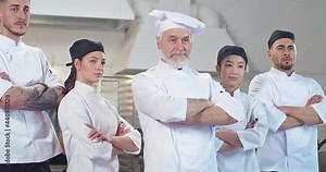 Portrait of mixed-race different young and senior professional chefs standing in kitchen posing together. Team of cooks in restaurant at work. Cooking industry, culinary, profession concept