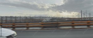 Side view through car window while driving on highway. View cars going in other lanes and distant bridges at sunset. Car driver's point of view.