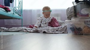 Cute baby girl playing with diaper while sitting on the floor in messy nursery room