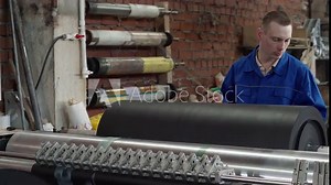 An engineer measuring the black fabric spinning on the manufacturing machine. Engineer checking the fabric roll on the manufacturing equipment. Engineer supervises the fabric manufacturing process.
