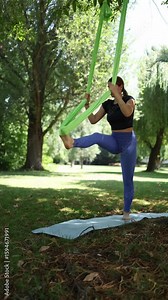 Vertical screen full-body extension and fierce control as woman stretches into standing split with aerial support holding pose with strength and precision in a sunlit forest glade