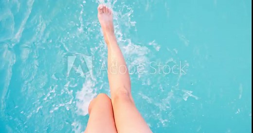 Barefoot female sunbathing playing feet in pure water at outdoor swimming pool
