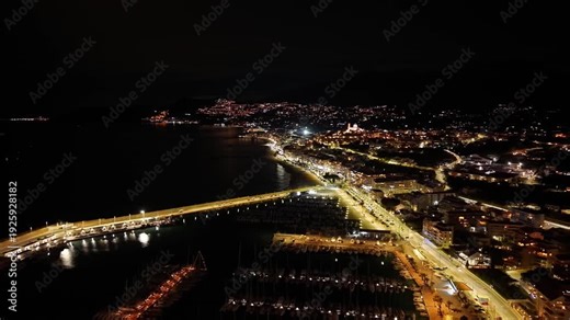 aerial night harbor lights sweeping coastal bay marina and bridge lit in golden glow, waterfront roads