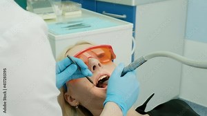 Close up female dentist hands in sterile gloves making treatment to patient using drill machine. Professional stomatologist in mask drilling teeth to female client. care, treatment. bur, tips