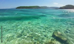 Tracking shot with gentle waves: A clear, coastal bay with gentle waves and transparent water. The camera tracks along the shoreline, highlighting the clear water and the gentle motion of the waves.
