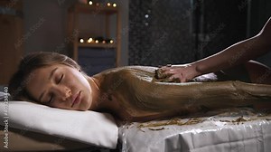 Wrapping the body of a young woman with seaweed and mud in a spa salon.
