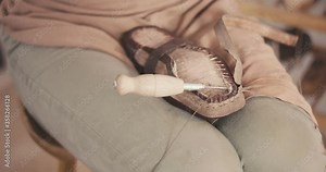 Traditional bespoke shoemaker tightens knot sewing stitching leather upper to insole on wooden shoe last with thread needle awl gloves on hands unrecognizable close up