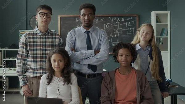 Medium portrait of multiethnic gen z students and their Black male programming teacher standing against chalkboard with written program algorithm and posing for camera