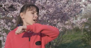 Allergic smell of flowers. A nice little girl smell the flowers and sneezing in the spring park.