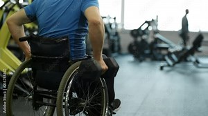 Tilt up with rear view of unrecognizable handicapped man in wheelchair doing one-arm dumbbell rows in gym