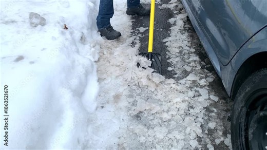 A thick sheet of ice being scraped off a car using an ice scraper after freezing rain. The scene demonstrates winter vehicle maintenance, icy conditions, and the challenges of cold weather driving