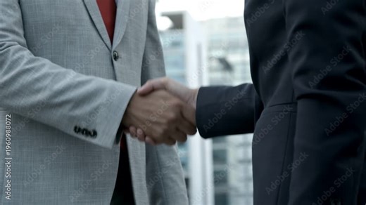 Two businessmen in professional suits share a corporate handshake in the office to celebrate a successful partnership agreement and teamwork deal
