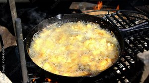 Boiling oil in cast iron pan over firepit while deep frying fish nuggets battered in breadcrumbs