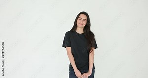 Young woman with long loose dark hair smiles and touching her chin on white background. Female model wearing black t-shirt and jeans