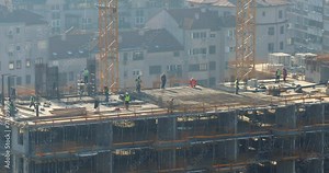 Construction workers labor on multi-story concrete building, telephoto view, time-lapse shot. High-level activities include formwork, reinforcement, and internal systems before concrete pouring.