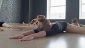 Medium long shot of little ballerinas in leotards doing stretching...