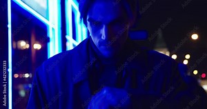 Drunk beared brunette man in a dark coat and in a hat walks down the street at the night. Blue light effect. Night city lights.