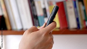 Digital Distraction: Scrolling vs. Reading. Hands scrolling through a smartphone with a library full of books in the background highlighting the contrast between time spent on social media and reading