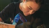 Close-up of young adult female tattooer, tattoo artist works with...