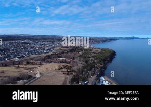 Wide-angle drone footage rising above the spring shoreline of Rimouski and the Sacr-Coeur district beside the St. Lawrence River under dramatic blue and cloudy skies in Quebec, Canada Stock Video Footage - Alamy