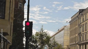 Red traffic light revealing from right to left behind a wall. Traffic light on the street surrounding by buildings and trees in Copenaghen, Denmark