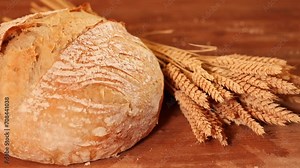 Slices of a delicious home made bread. Bread baking 4k video in a beautiful setup with ears of wheat in background. Fresh bread on the wooden counter top next to ears of wheat. View from above.