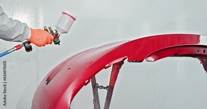 Auto body technician spray painting a red car bumper in a specialized chamber. Highlighting automotive repair and paint services in a professional garage. Painting Car in Workshop