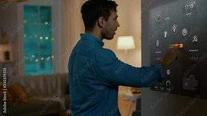 Handsome Young Man Interacts with Augmented Reality Display. He is Turning On the Lights in His Cozy Flat. Young Couple in Smart Home Concept with Transparent Screen Made with VFX Special Effects.