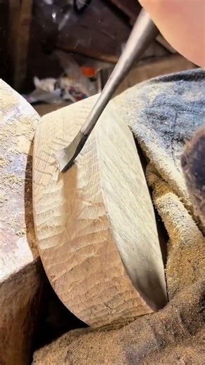 carving the side of a thick wooden block using a manual chisel to create a rough curved surface