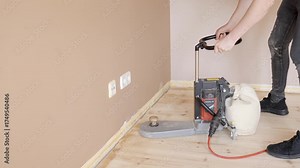 Edge sander smoothing wooden floor along baseboard inside residential room, medium static