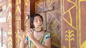 Pretty young woman plays flute before artistic village door. Close up. Slow track around left