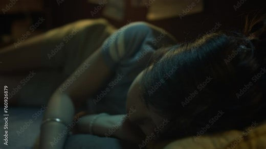 Medium close-up footage of young Chinese woman lying on bed in bedroom in evening, watching TV, then turning to side and going to sleep