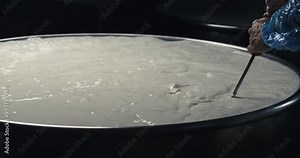 Super slow motion close up of artisan cheesemaker is mixing fresh bio eco milk during traditional cheese making process at cheese production creamery dairy factory at 1000 fps.