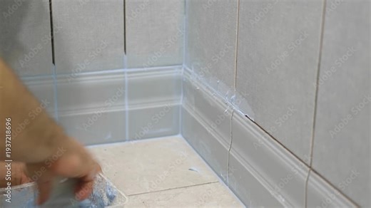 Worker using a rubber grout float to smooth grout between tiles. Carefully applying sealant to tiles joints. Workman hands smoothing caulk, using small tool to remove excess and create clean seam.