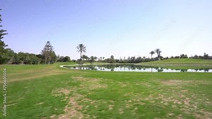 Agadir, Morocco - February 25, 2024 - Golf course view with a water hazard reflecting surrounding trees under a bright blue sky, and lush green fairways.