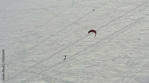Riding the kite on the ice of big lake. Athletes rides a kite in the winter. Catch wind. Concept of winter sports snowkite on ski.