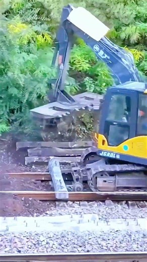 Hydraulic arm grips steel rail—worker watches as gravel shifts beneath machine’s precise force.