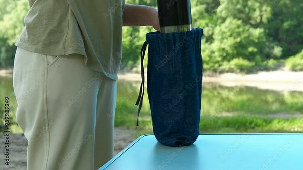 Woman hand with thermos on outdoor table. A view of woman put his thermos on the table during picnic time.