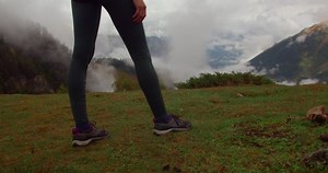 Young adventurous woman hiking on mountain top above the clouds, active traveler walking in highland